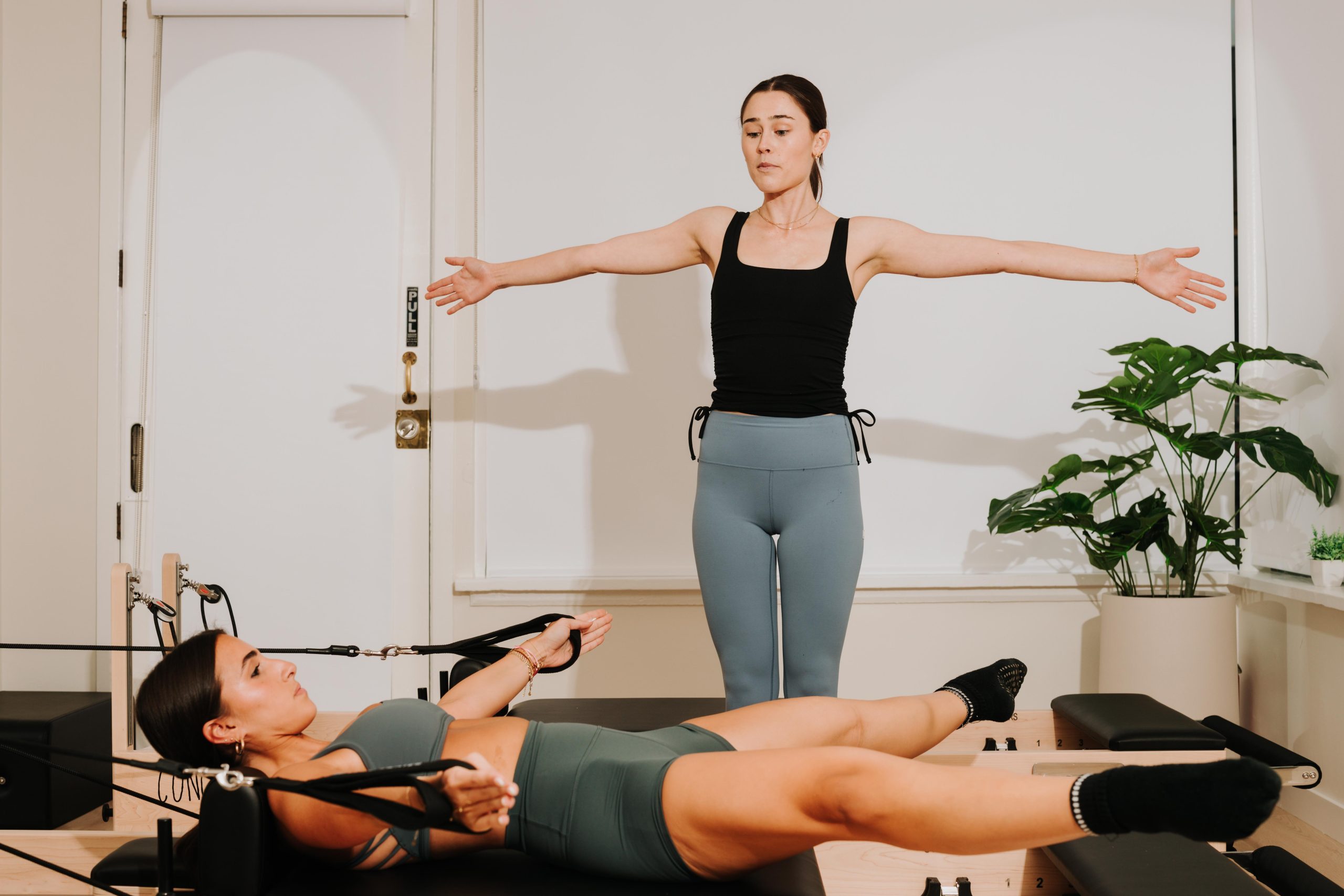 An instructor watching a member hold a position on the reformer at YA FIT Pilates Tarzana
